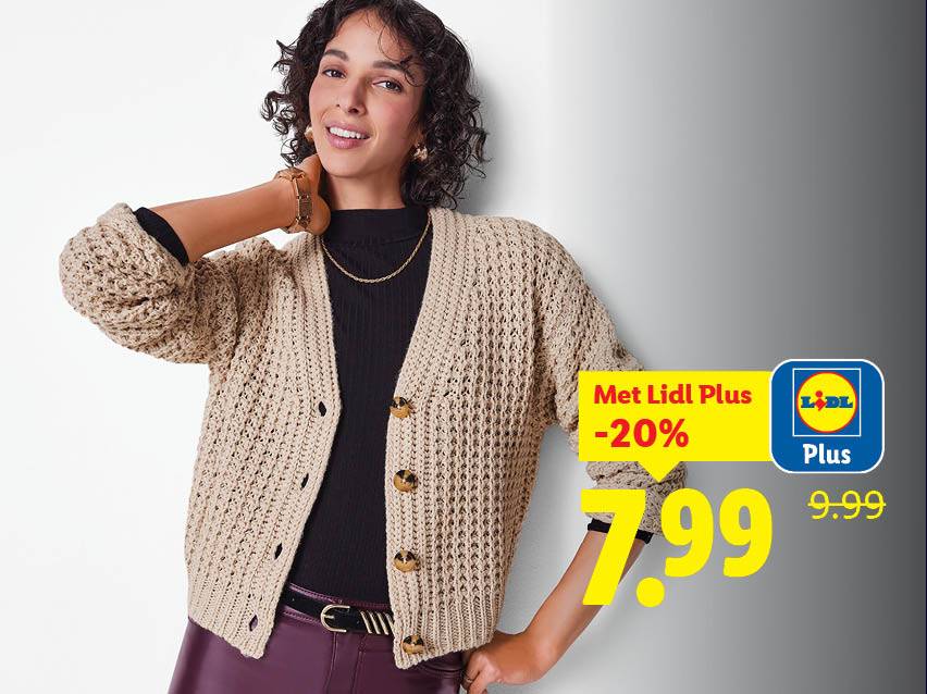 Een lachende vrouw draagt een beige gebreid vest, een zwarte coltrui en een bordeauxrode broek.