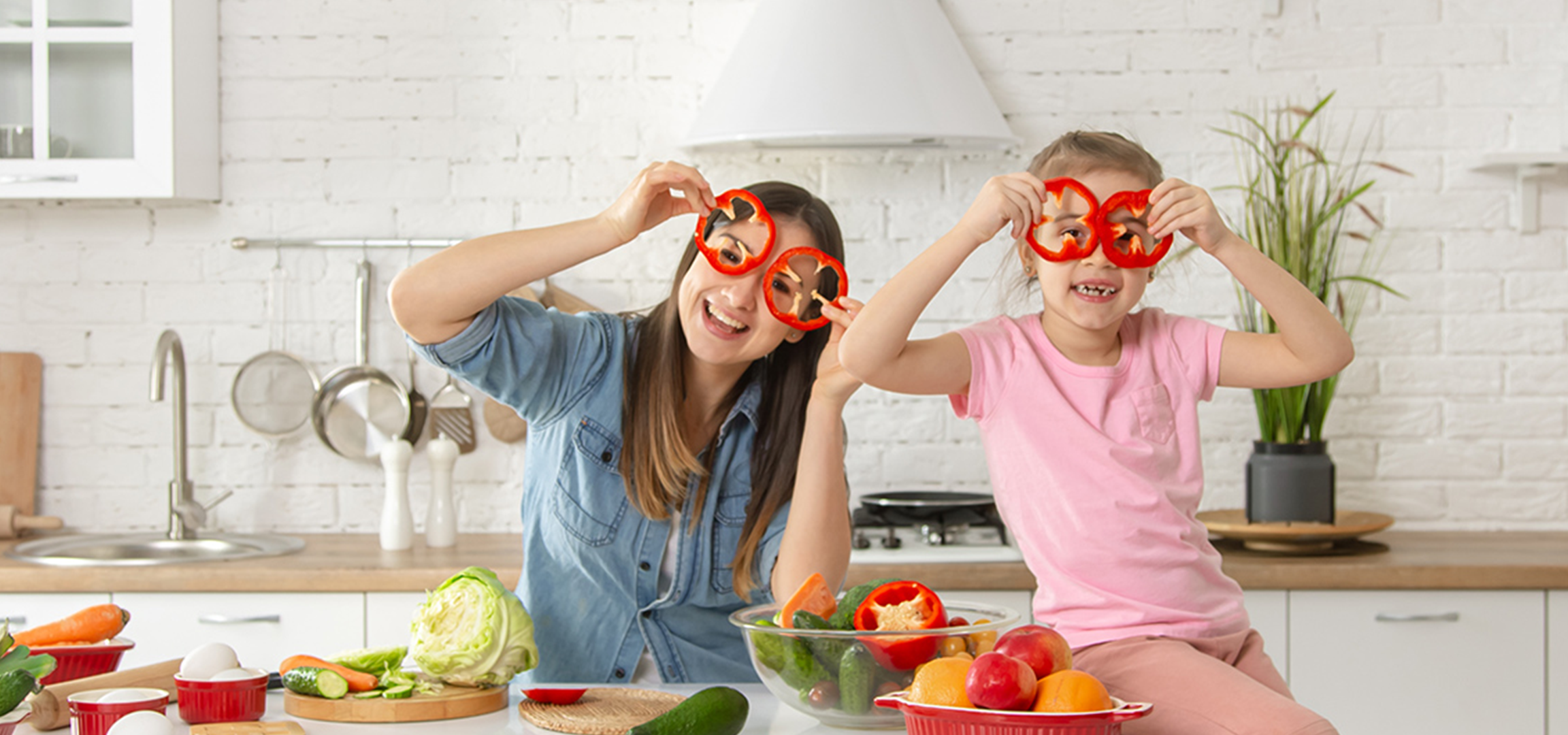 Une mère et sa fille s'amusent en cuisine avec des tranches de poivron rouge comme des lunettes.