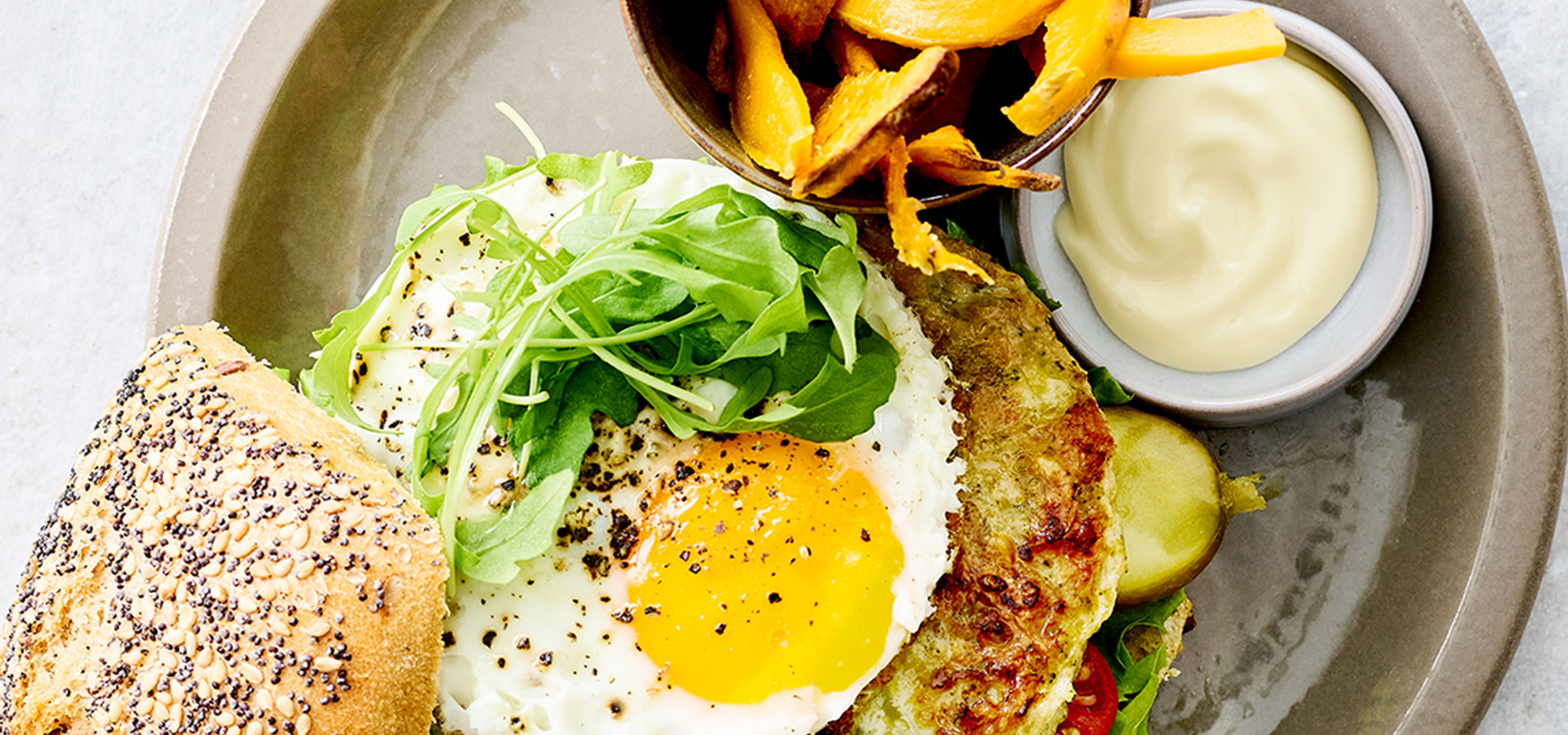 Een heerlijke burger op een broodje met gebakken ei, rucola en zoete aardappel frietjes.