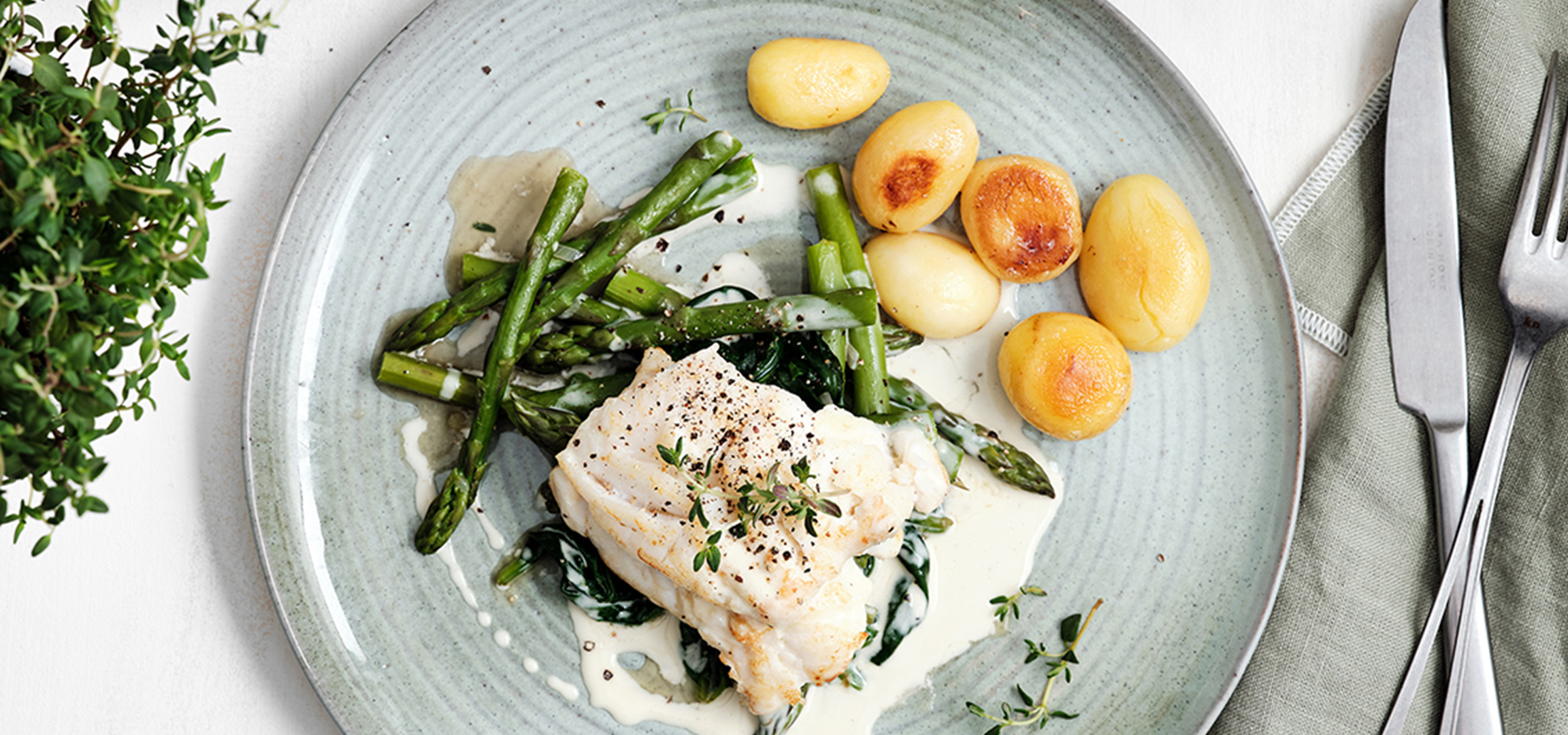 Poisson blanc en sauce crémeuse, servi avec asperges et pommes de terre.