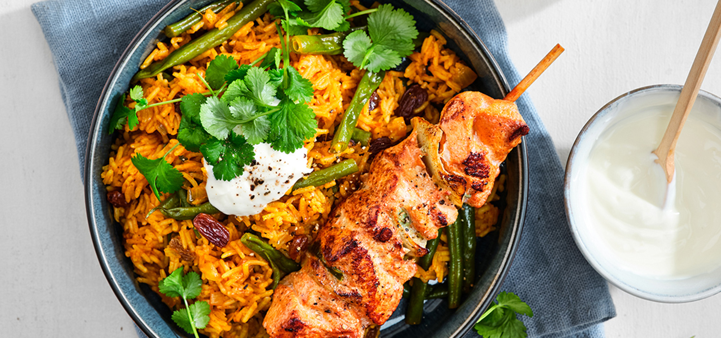 Een gerecht met saffraanrijst, gegrilde kipsaté, groene bonen en yoghurt.