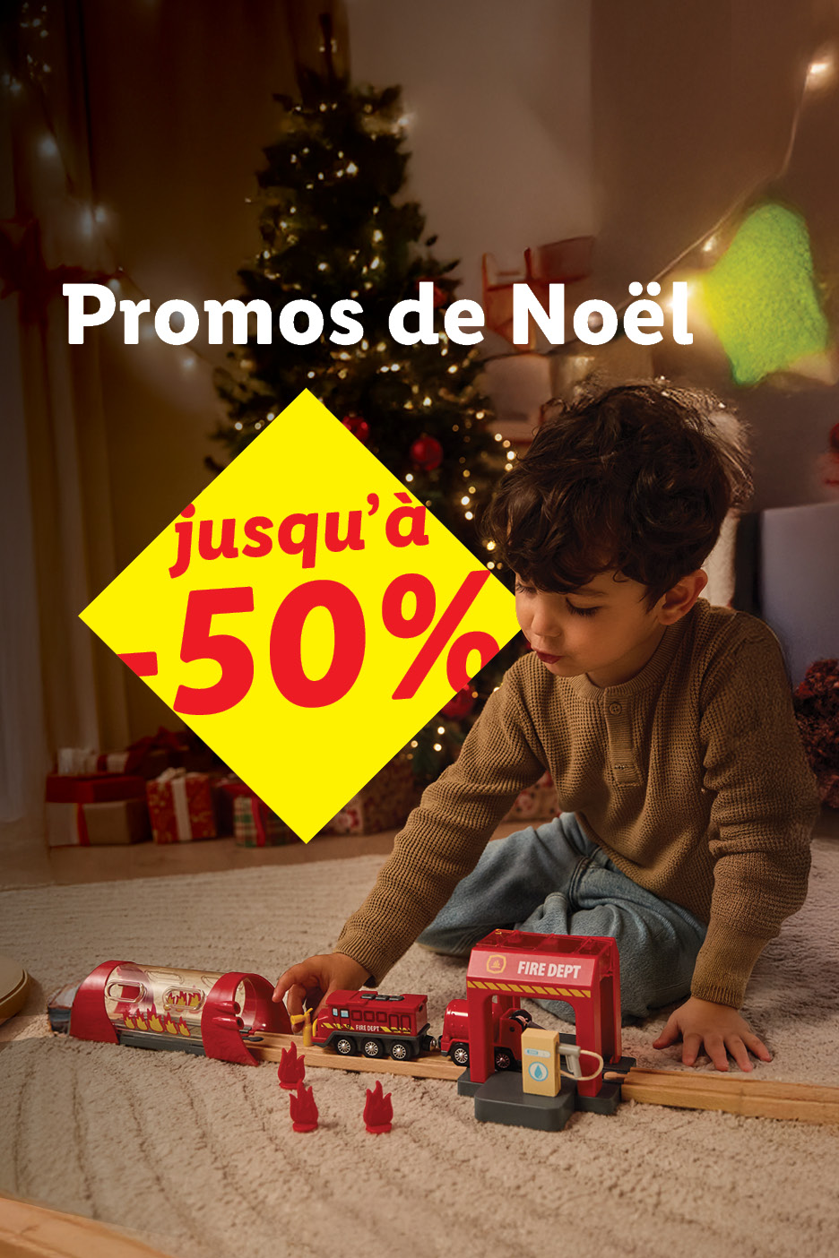Garçon joue avec un train en bois et une caserne de pompiers, promos de Noël jusqu'à -50%.