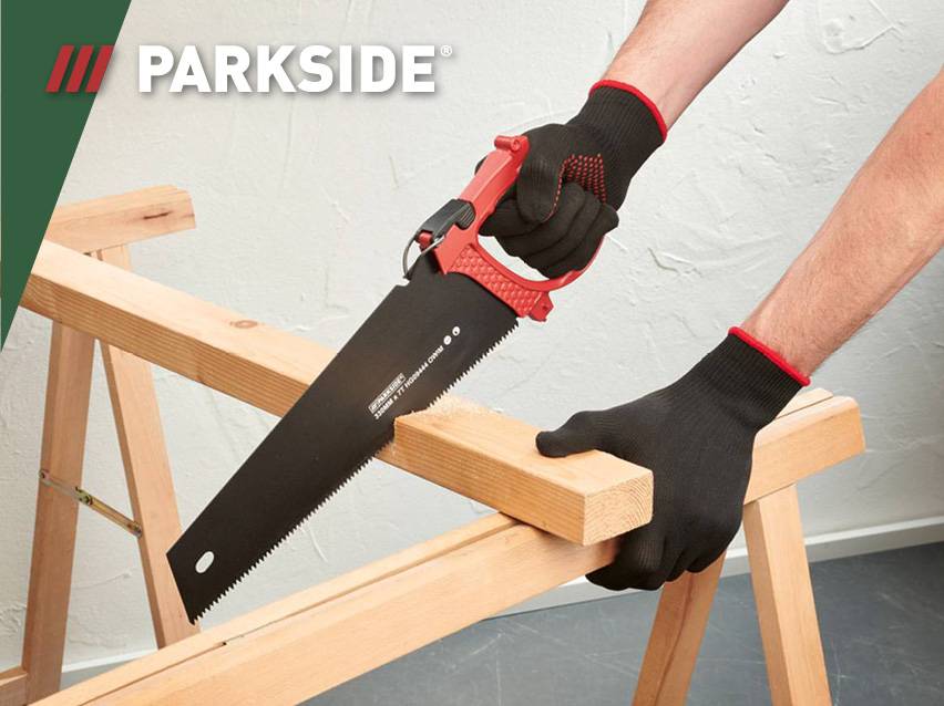 Een persoon met zwarte handschoenen zaagt een houten plank met een Parkside zaag.