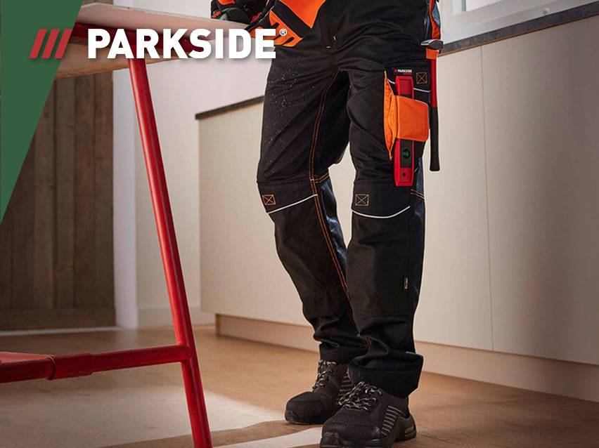 Een persoon draagt zwarte werkbroeken met oranje accenten en gereedschap.