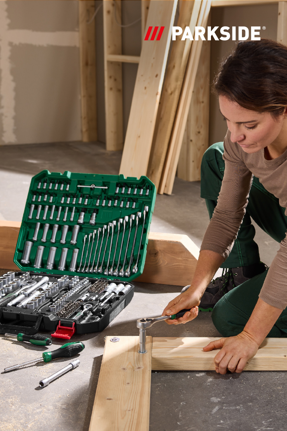 Vrouw monteert houten frame met een dopsleutelset, met een grote gereedschapskist ernaast.