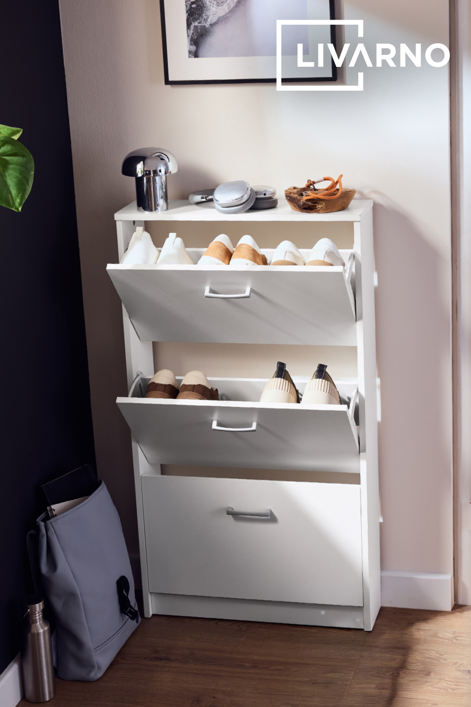 Witte schoenenkast met drie lades, gevuld met schoenen, in een hal.