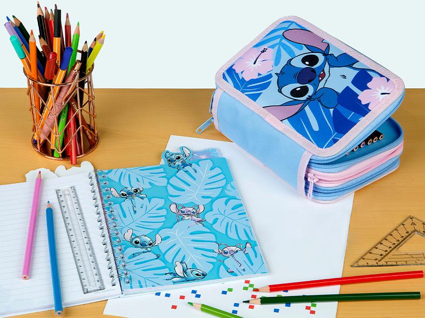 Bureau met een etui en notitieboekje met blauwe monstera-bladeren en een buitenaards wezen, en een pennenhouder.
