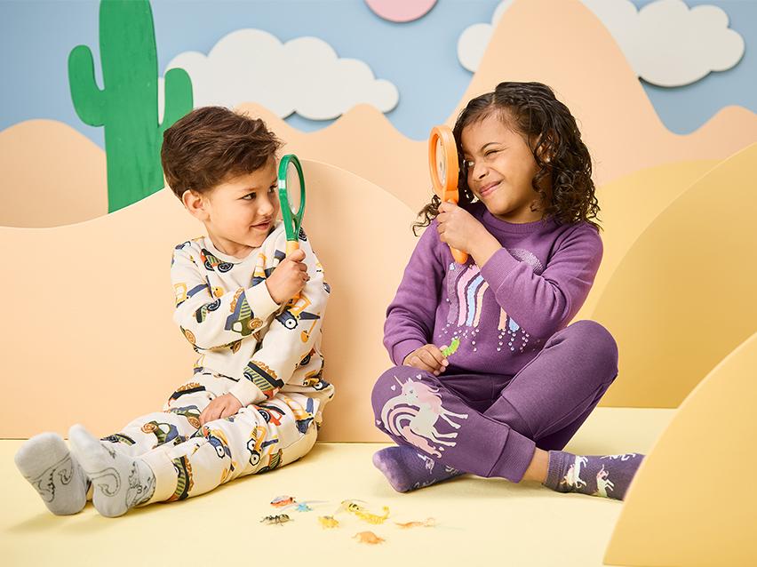 Twee kinderen in pyjama met vergrootglazen, spelend met speelgoedinsecten.