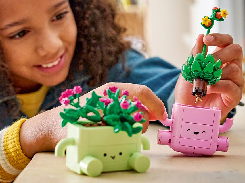 Een lachend meisje speelt met bouwstenen bloempotten, één groen en één roze.