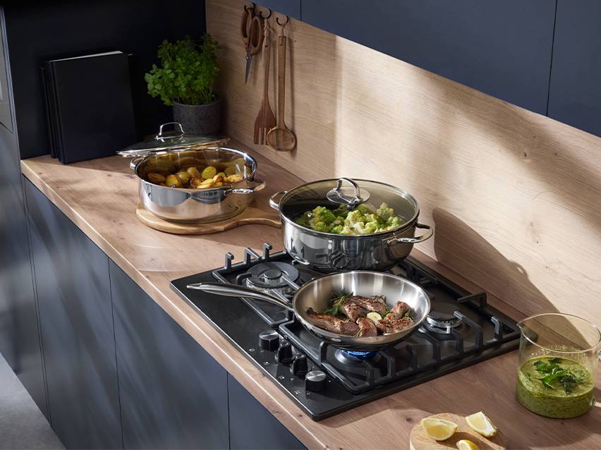 Moderne keuken met roestvrijstalen pannen op een gaskookplaat en een houten aanrecht.