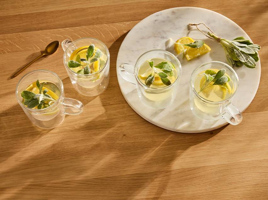 Vier kopjes citroen-salie thee op een houten tafel en marmeren dienblad.