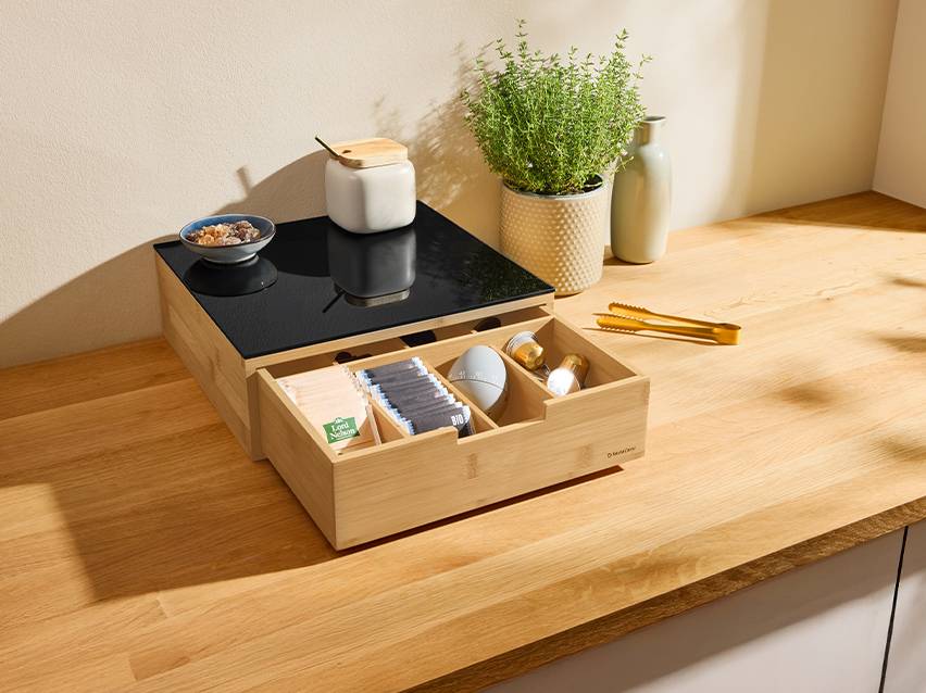 Houten theedoos met lade vol theezakjes en koffiecapsules op een aanrecht.