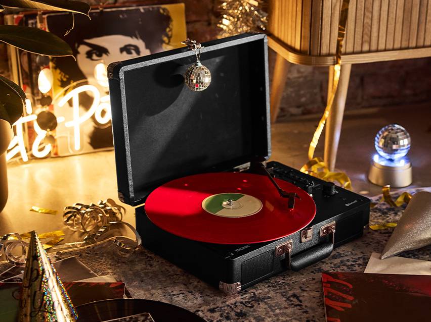 Zwarte draagbare platenspeler met een rode plaat, omringd door feestdecoraties.