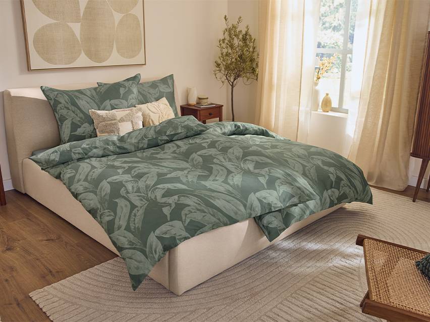 Slaapkamer met groen dekbedovertrek met bladprint, beige bed en vloerkleed.
