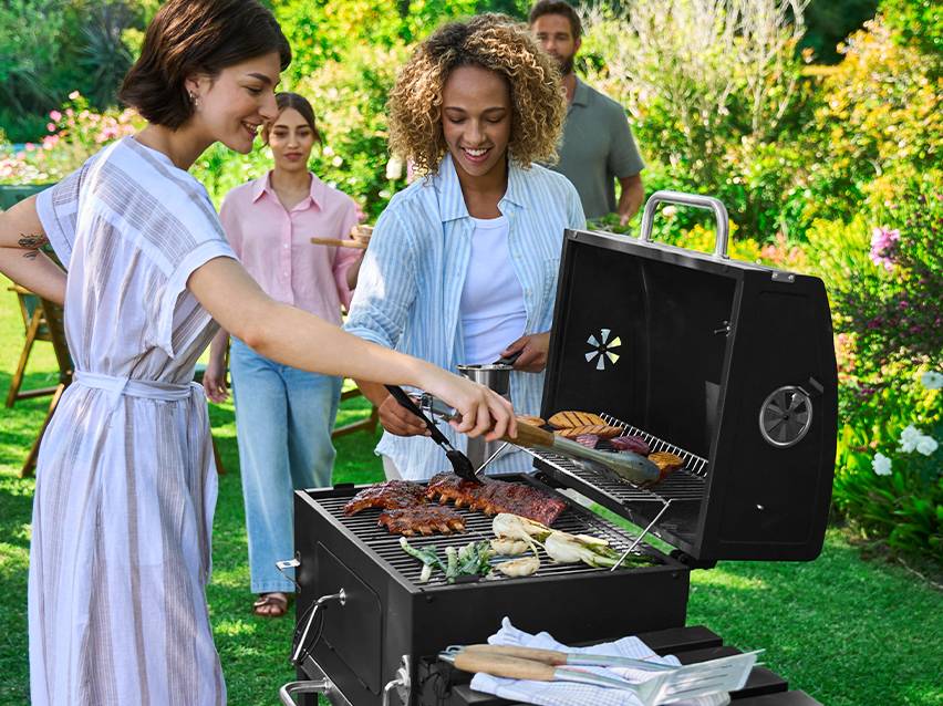 Vier vrienden barbecueën in de tuin met vlees en groenten op de grill.