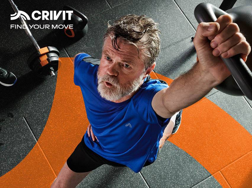 Homme barbu en t-shirt de sport bleu s'entraînant avec des équipements de fitness.