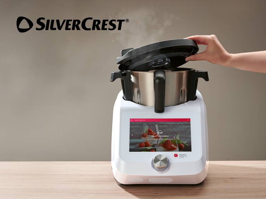 Witte multifunctionele keukenmachine met touchscreen, deksel opgetild, op een houten tafel.