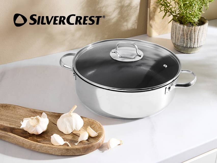 Roestvrijstalen kookpan met glazen deksel op een aanrecht met knoflook.