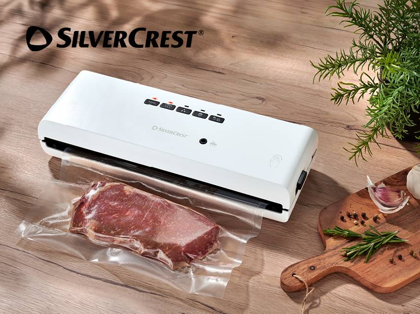 Witte vacuümsealer met een verpakt stuk vlees, kruiden en knoflook op een houten tafel.