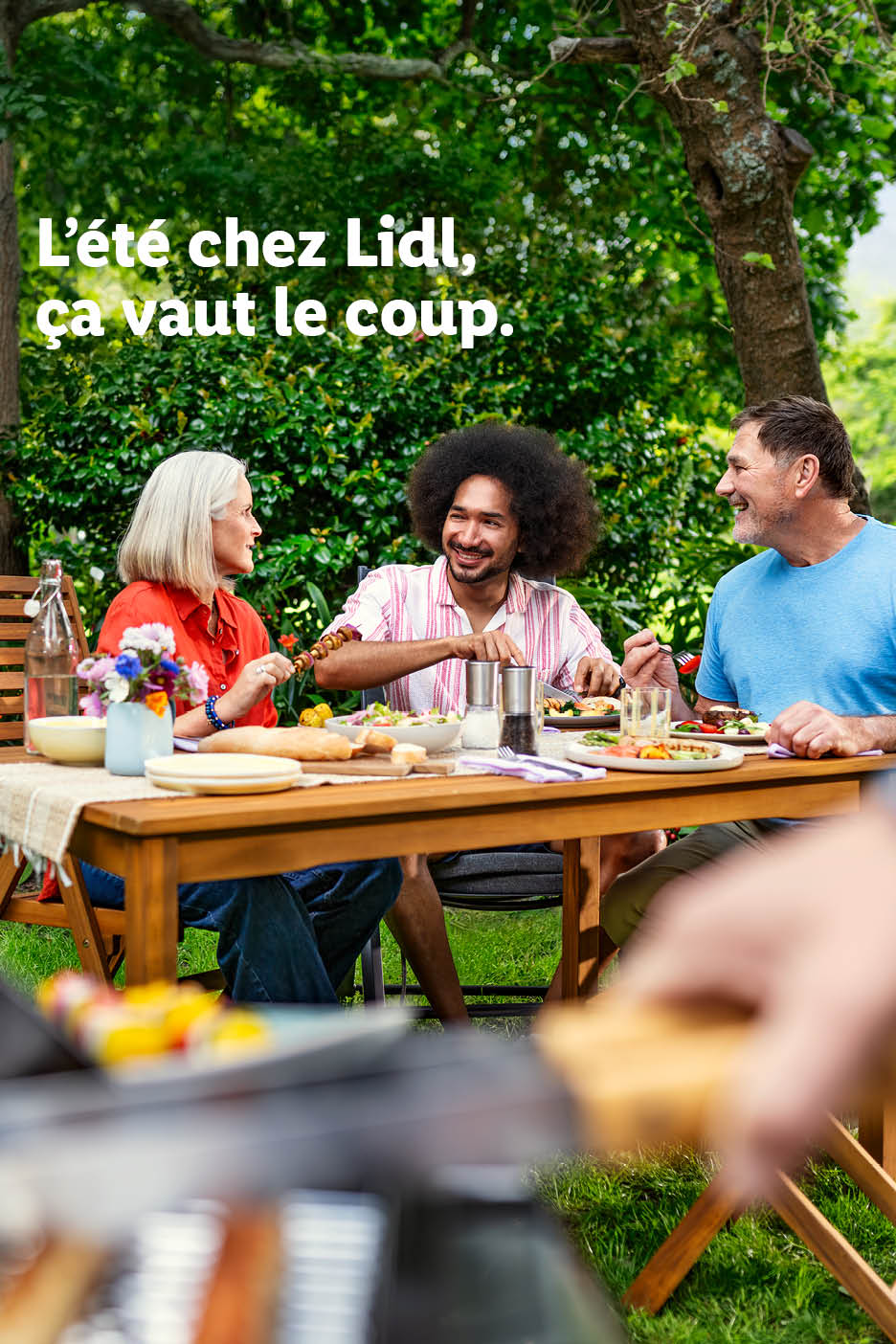Zomerse barbecue met vrienden en familie, met salades, brood en vleesspiesen. Tekst: 'De zomer bij Lidl is de moeite waard.'