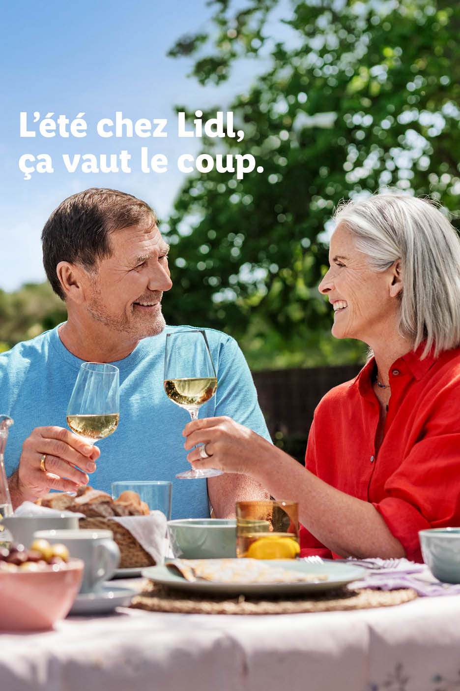 Zomerse maaltijd buiten met een ouder stel dat lacht en witte wijn drinkt. Tekst: 'De zomer bij Lidl is de moeite waard.'