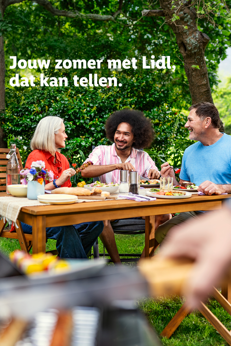 Zomerse barbecue met vrienden in de tuin, met salades, brood en vleesspiesen. Tekst: Jouw zomer met Lidl, dat kan tellen.