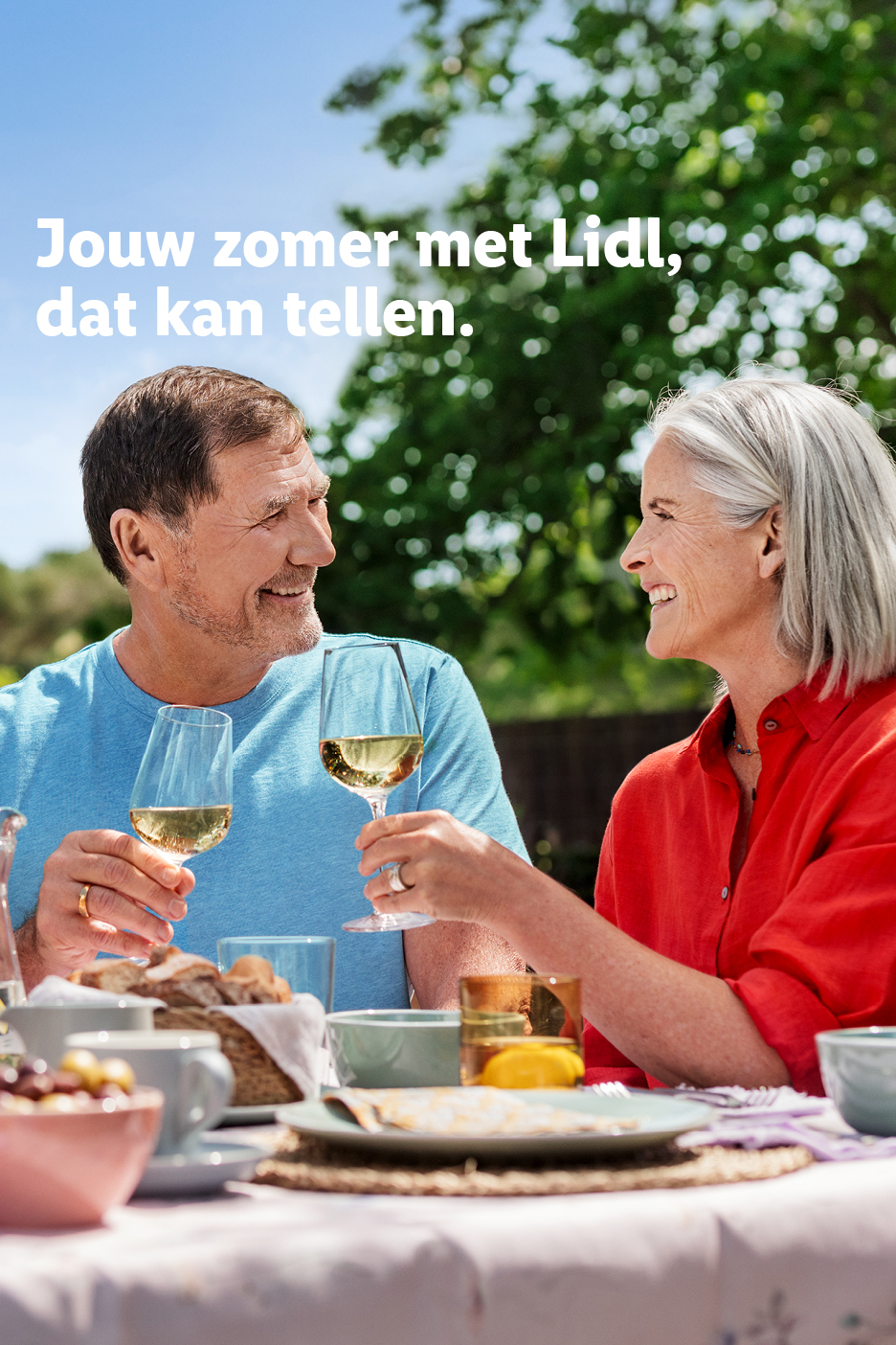 Zomerse maaltijd buiten met een ouder stel dat proost met witte wijn. Tekst: Jouw zomer met Lidl, dat kan tellen.