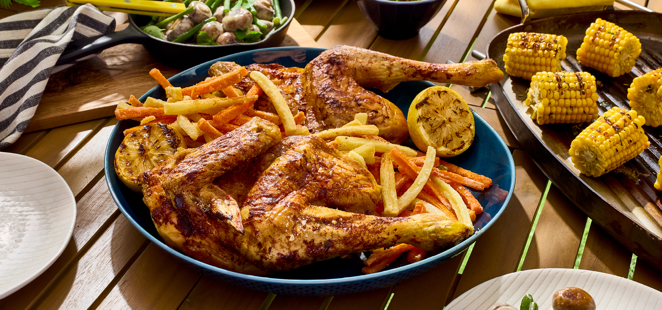 Geroosterde kip met frietjes en gegrilde maïs op een houten tafel.
