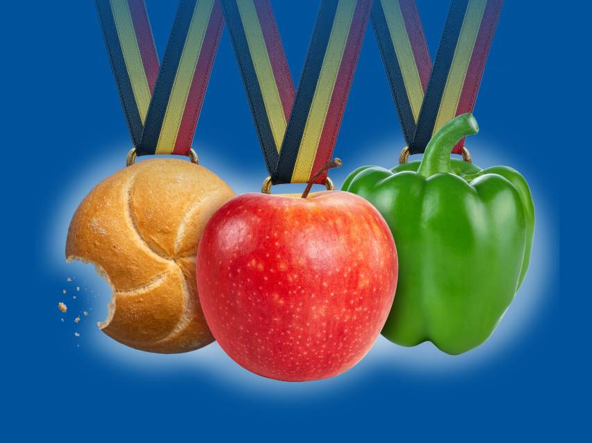 Drie medailles met een aangebeten broodje, een rode appel en een groene paprika op blauwe achtergrond.