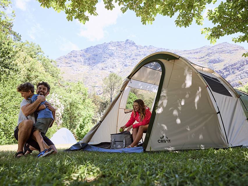 Familie kampeert met een tent en koeltas, in een bergachtig landschap.
