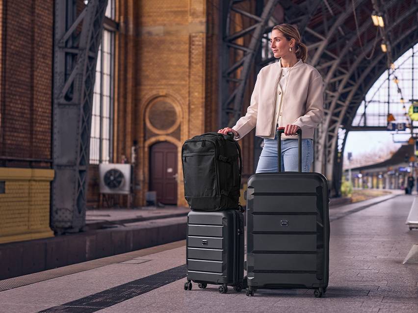 Vrouw met een rugzak en twee zwarte koffers op een treinstationperron.