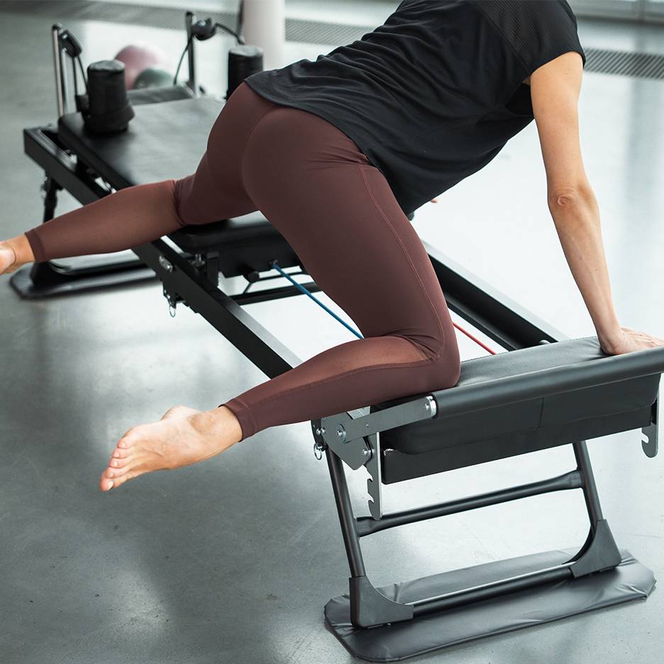 Vrouw oefent op een Pilates-apparaat, gericht op benen en billen.