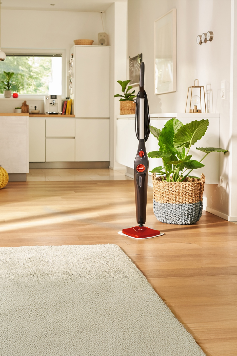 Een rode en zwarte Vileda stoommop in een moderne keuken met een houten vloer.