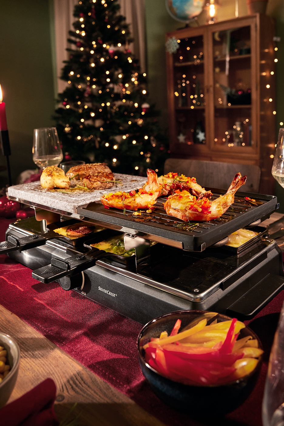 SilverCrest raclette met grillplaat, steenplaat, garnalen en vlees op een feestelijk gedekte tafel.