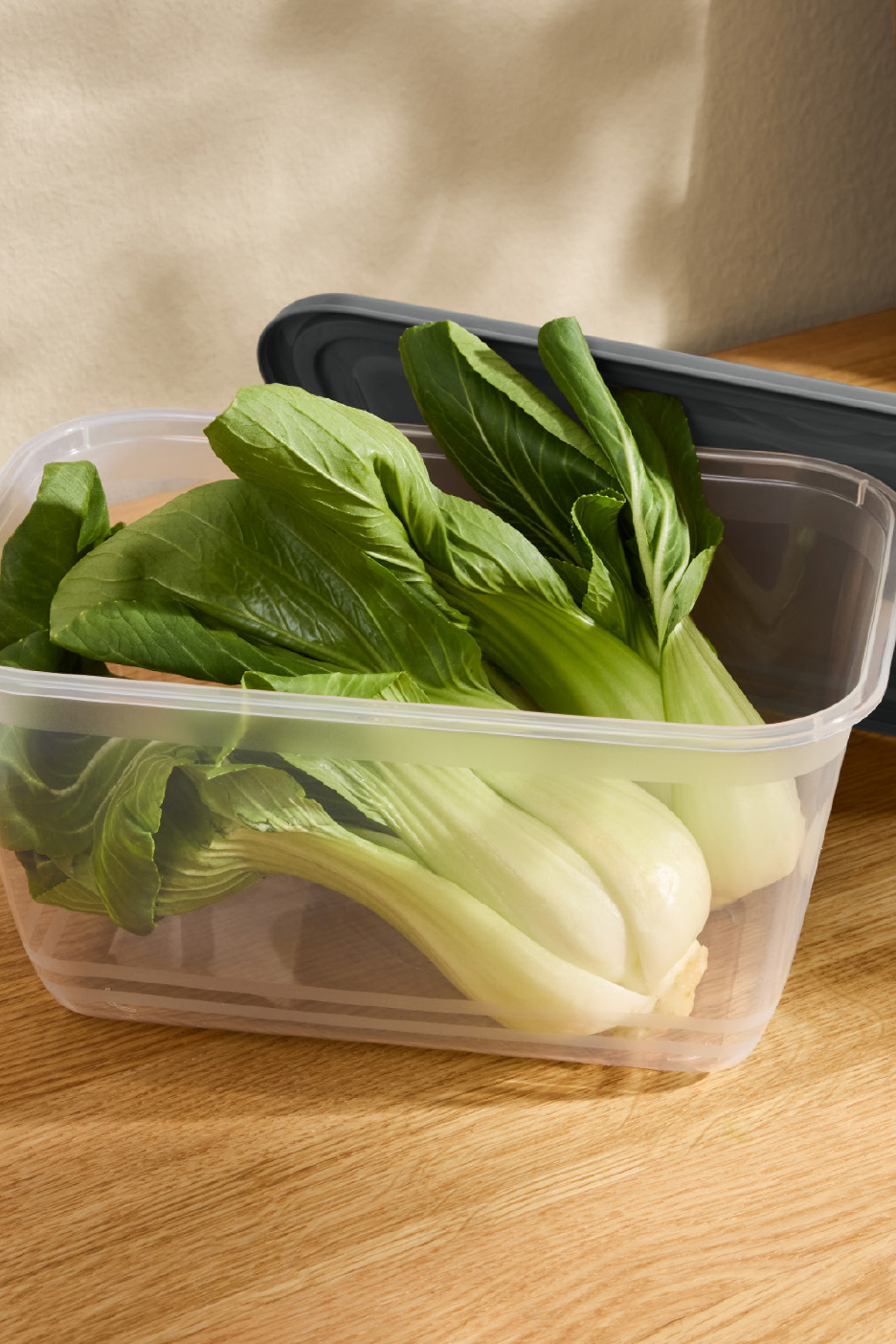 Verse paksoi in een transparante vershouddoos op een houten tafel.