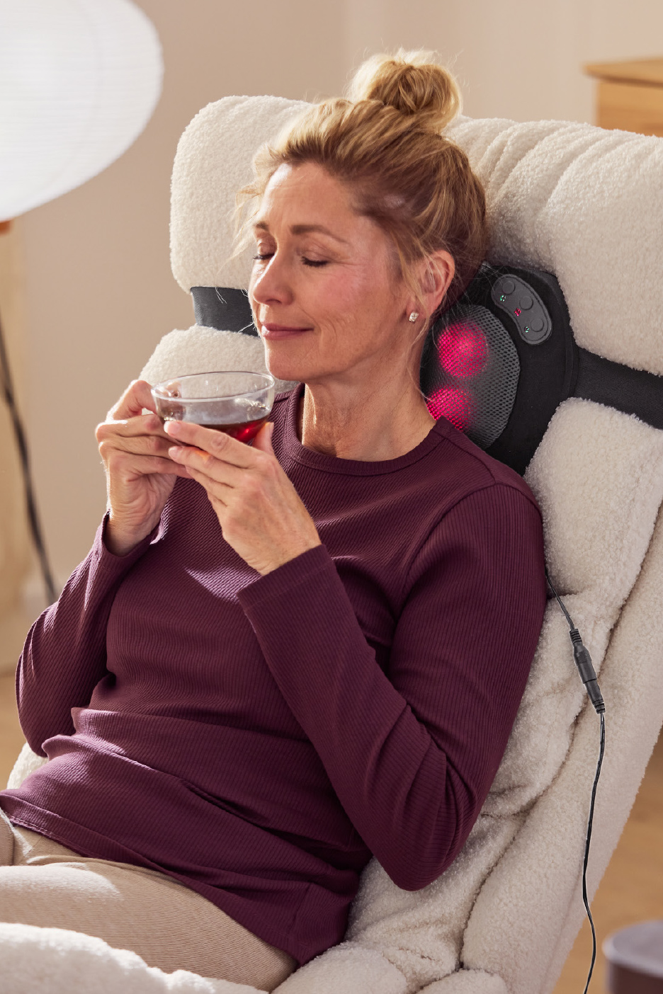 Vrouw ontspant in een massagestoel met een kopje thee.