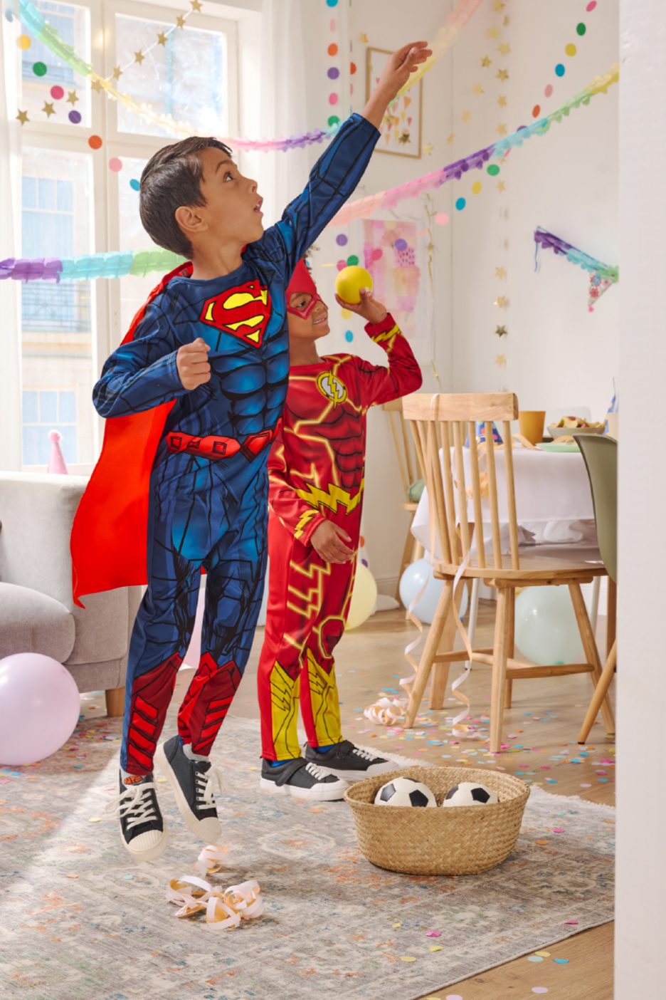 Twee jongens in superheldenkostuums spelen op een feestje met slingers en confetti.