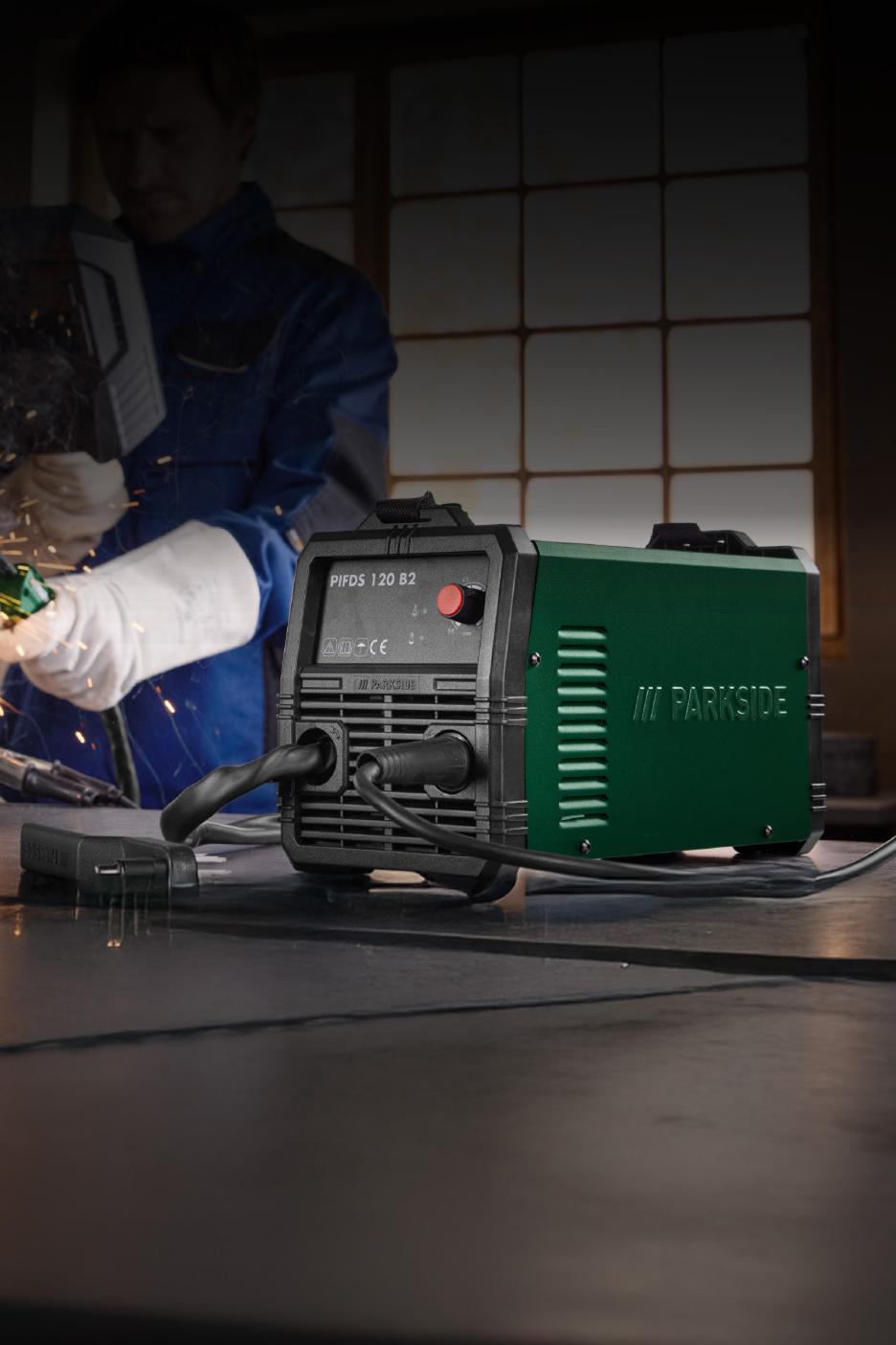 Een groen-zwart lasapparaat op een tafel, met een lasser op de achtergrond.