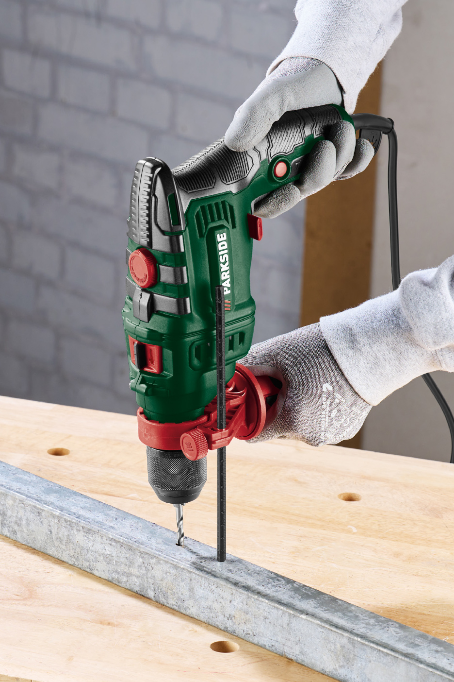 Groene en zwarte klopboormachine met snoer, gebruikt om een metalen profiel op een houten werkbank te boren.