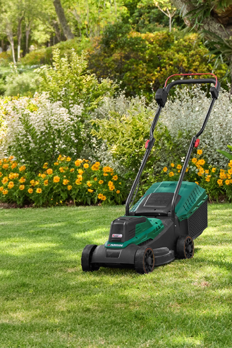 Een grasmaaier op een groen gazon met bloeiende struiken en bomen op de achtergrond.