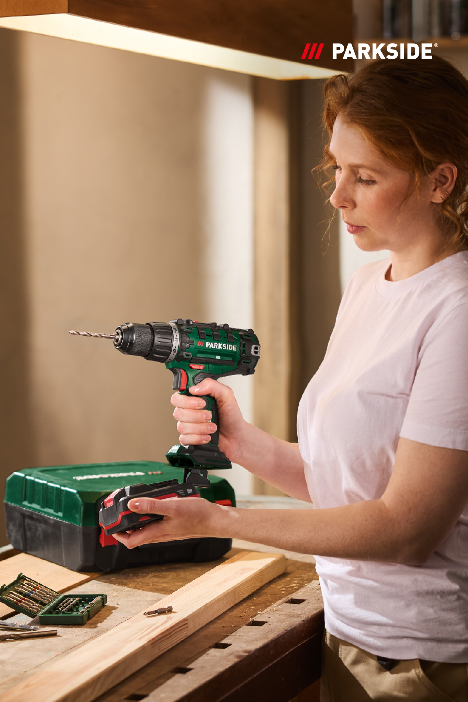 Vrouw met een boormachine en een accu in haar handen, klaar om te klussen.