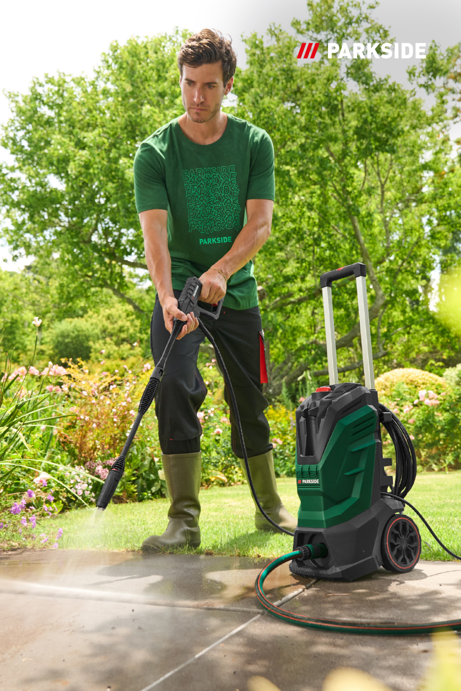 Man reinigt terras met hogedrukreiniger in een groene tuin.