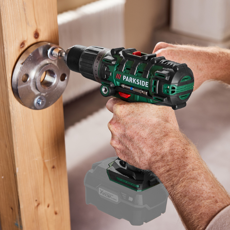 Een man gebruikt een accuboormachine om een metalen flens aan een houten balk te bevestigen.