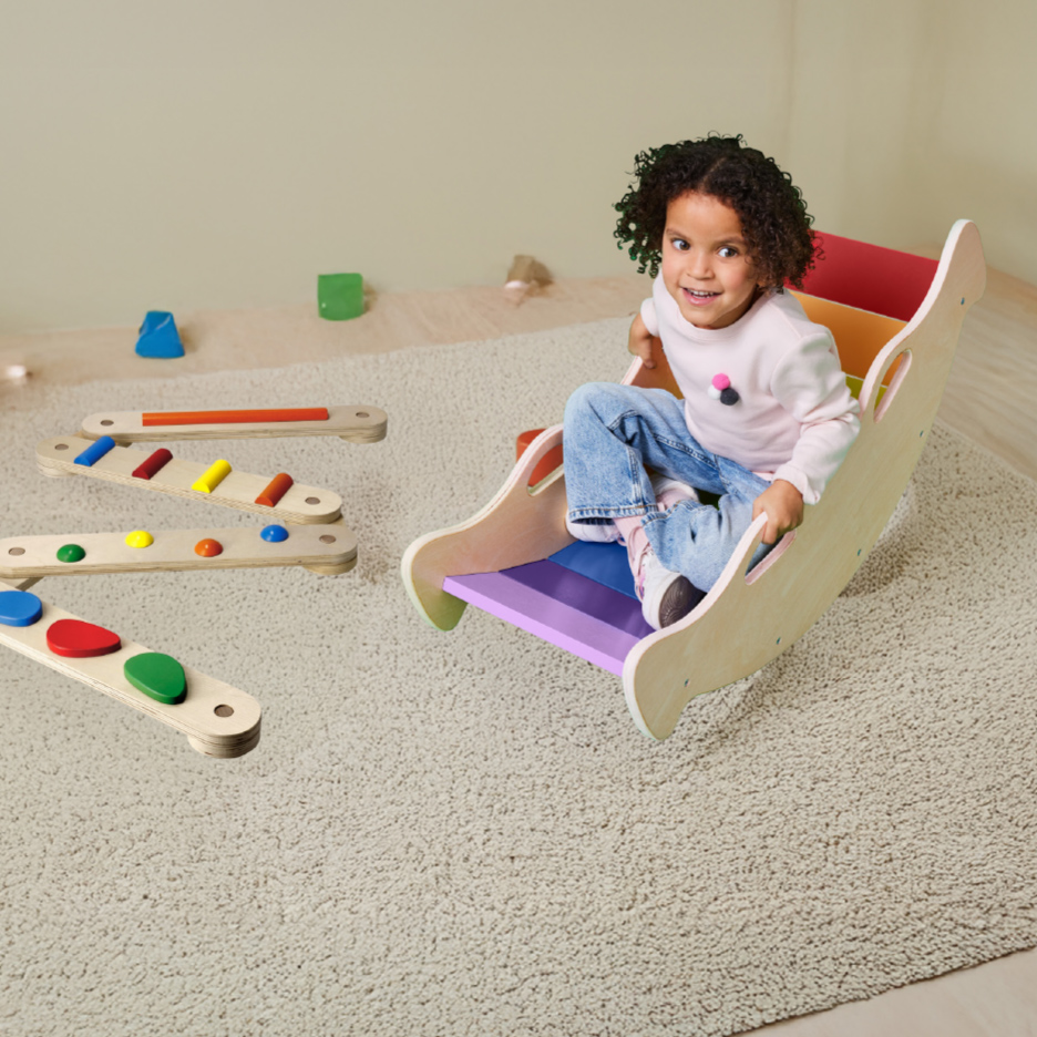 Lachend kind op regenboogwipstoel, met houten balansspeelgoed op een tapijt.