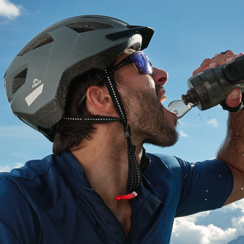 Fietser met helm en zonnebril drinkt water uit een bidon.
