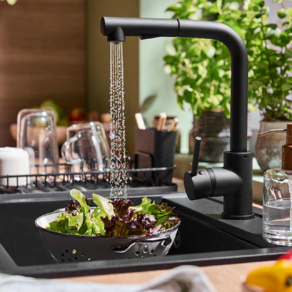 Zwarte keukenkraan met uittrekbare sproeier wast sla in een gootsteen.