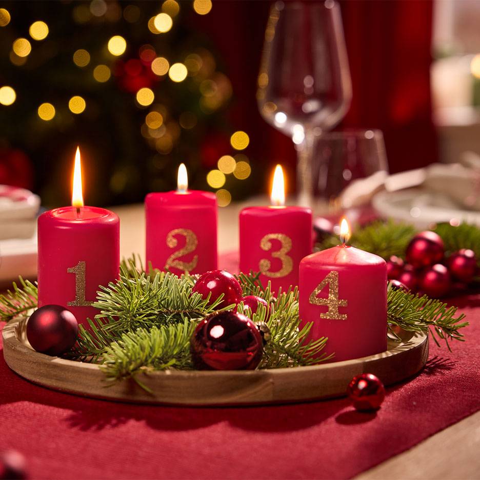 Adventskrans met vier rode kaarsen genummerd 1 tot 4, omringd door dennentakken en kerstballen.