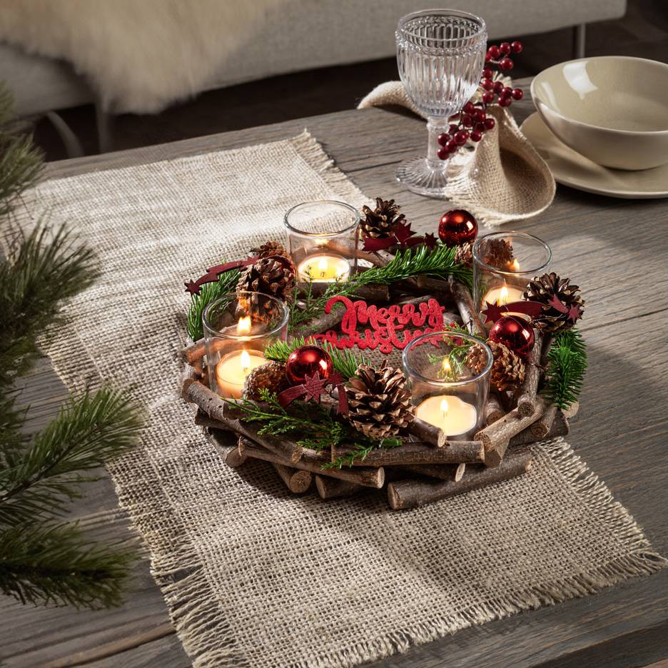 Kersttafeldecoratie met kaarsen, dennenappels en dennentakken op een rustieke houten schaal en jute tafelloper.