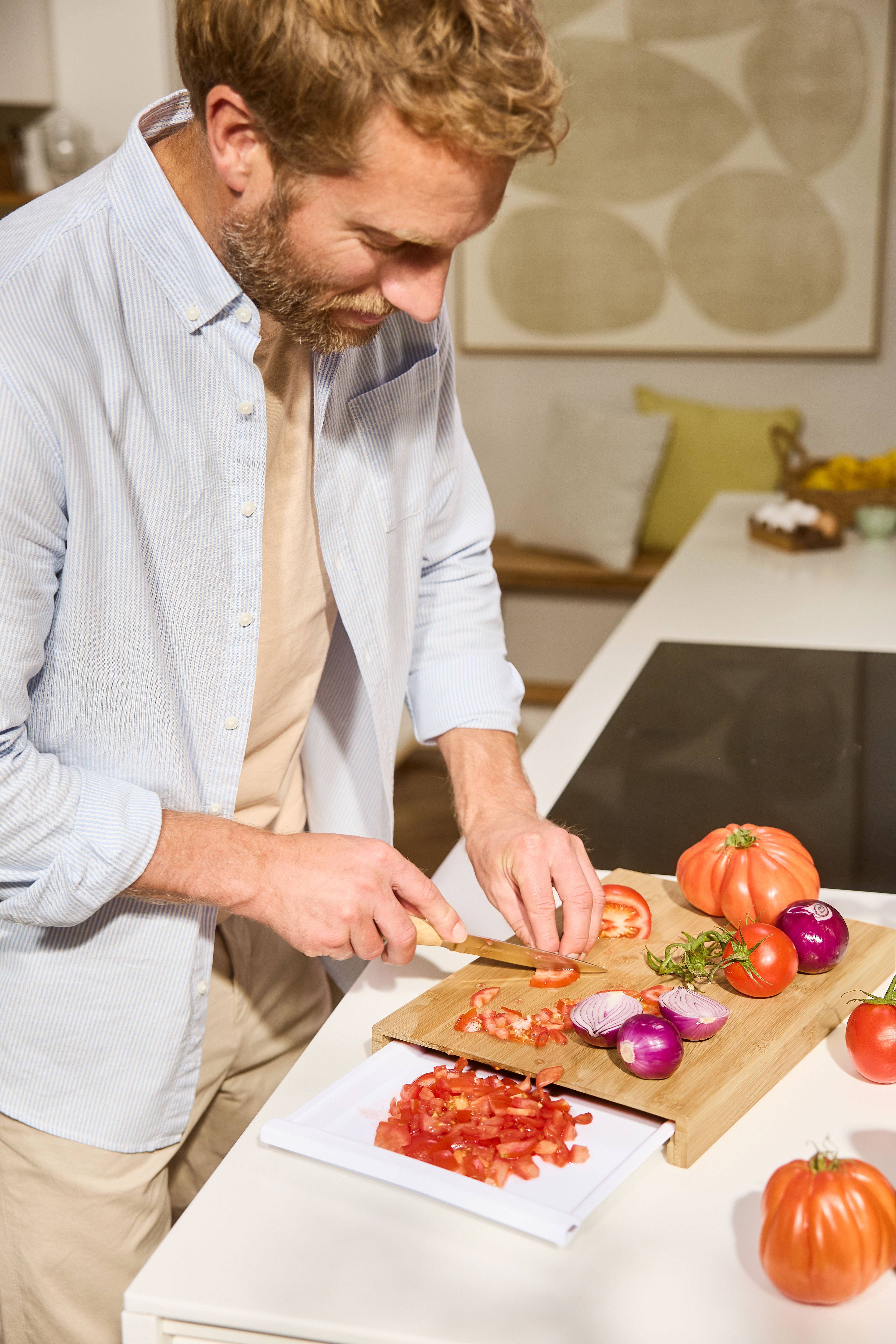 Man snijdt tomaten en uien op een houten snijplank in de keuken.