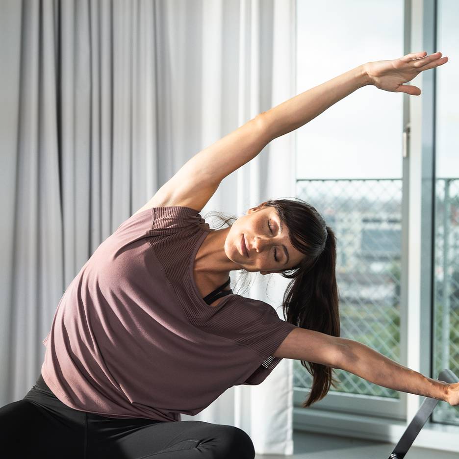 Vrouw sport in sportshirt en zwarte legging, rekt zich uit met gesloten ogen.